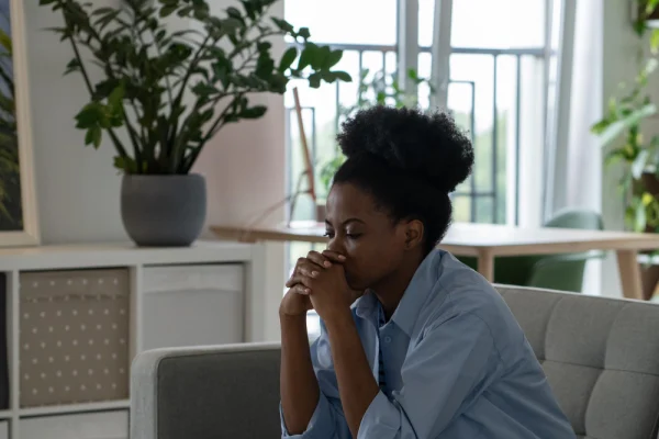 Oppressed African American woman with sad face sits on sofa thinking about future Life trouble