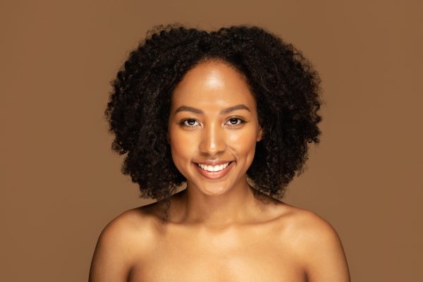 Natural Beauty Concept. Headshot of cheerful smiling attractive young black woman with bushy hair posing naked on colorful studio background, free from artificial enhancements